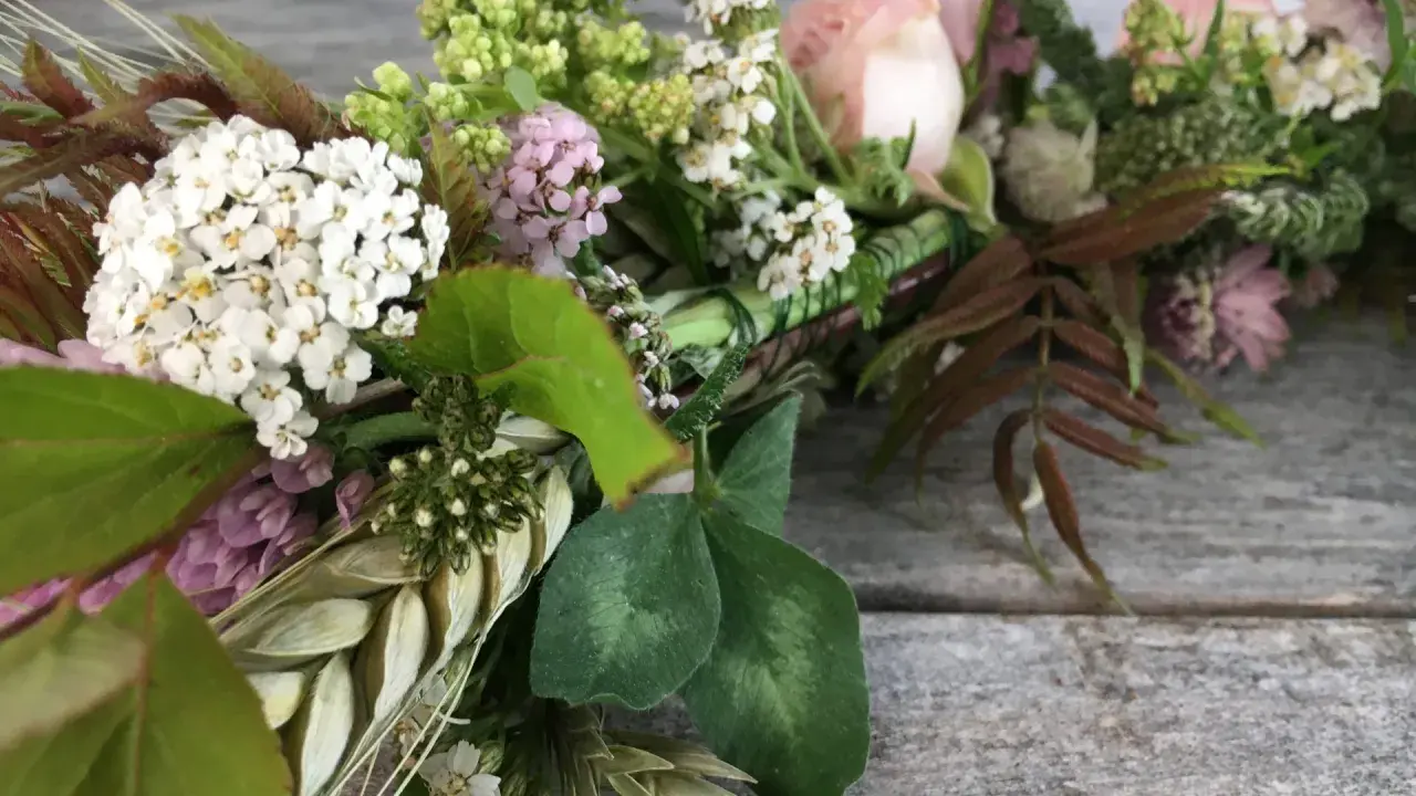 Vacker krans med vita och rosa blommor, gröna blad och ax. Någon har valt att binda krans med kärlek.