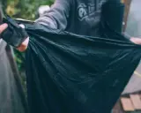 En person håller upp en stor, svart, nedbrytbar markduk. Den är skrynklig och verkar vara gjord av ett tunt material.