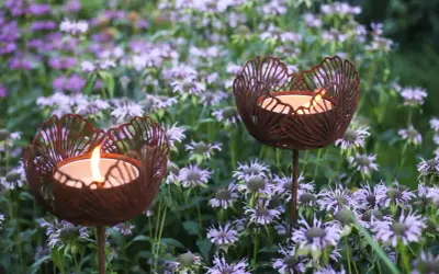 Två rostiga ljushållare i form av blommor lyser upp en rabatt med lila blommor.