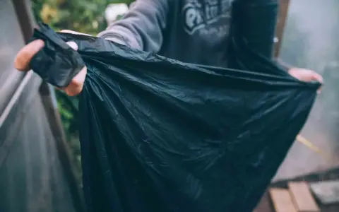 En person håller upp en stor, svart, nedbrytbar markduk. Den är skrynklig och verkar vara gjord av ett tunt material.
