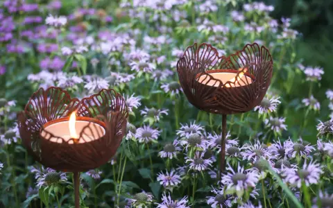 Två rostiga ljushållare i form av blommor lyser upp en rabatt med lila blommor.