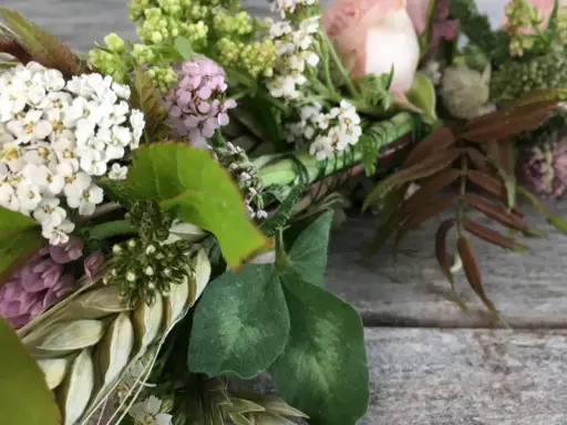Vacker krans med vita och rosa blommor, gröna blad och ax. Någon har valt att binda krans med kärlek.