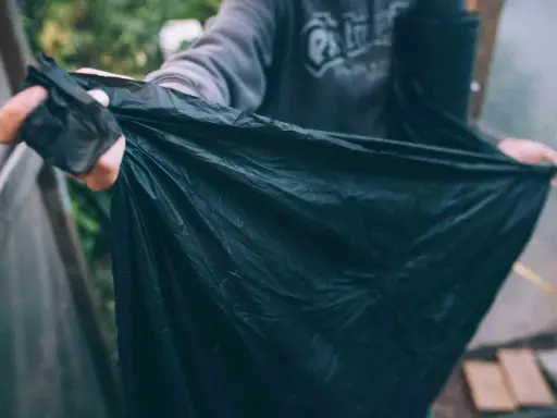En person håller upp en stor, svart, nedbrytbar markduk. Den är skrynklig och verkar vara gjord av ett tunt material.