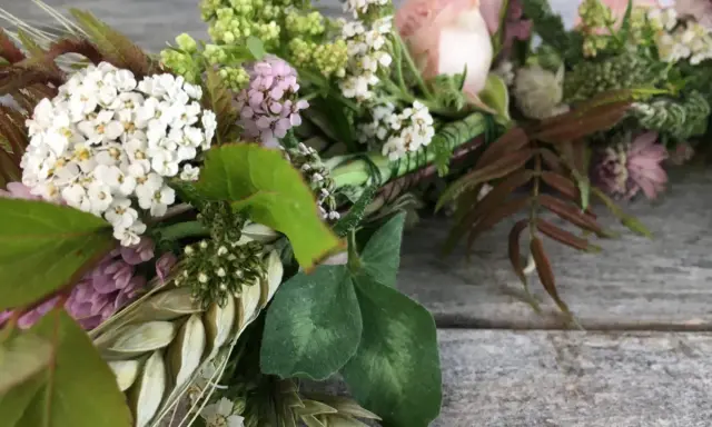 Vacker krans med vita och rosa blommor, gröna blad och ax. Någon har valt att binda krans med kärlek.