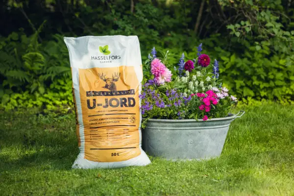 En säck Hasselfors U-jord bredvid en zinkbalja fylld med färgglada blommor i kruka.